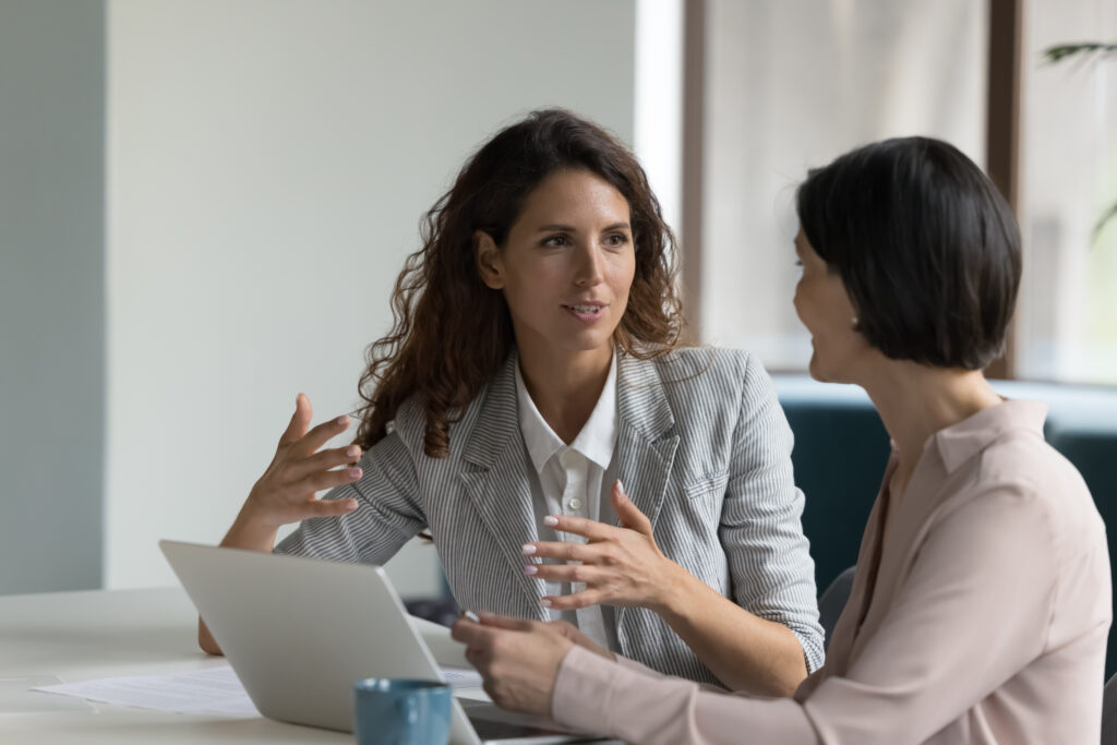 Two businesswomen sit at desk discuss project details